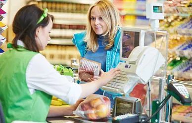 Cliente pagando en la caja de un supermercado mientras el cajero escanea los artículos.