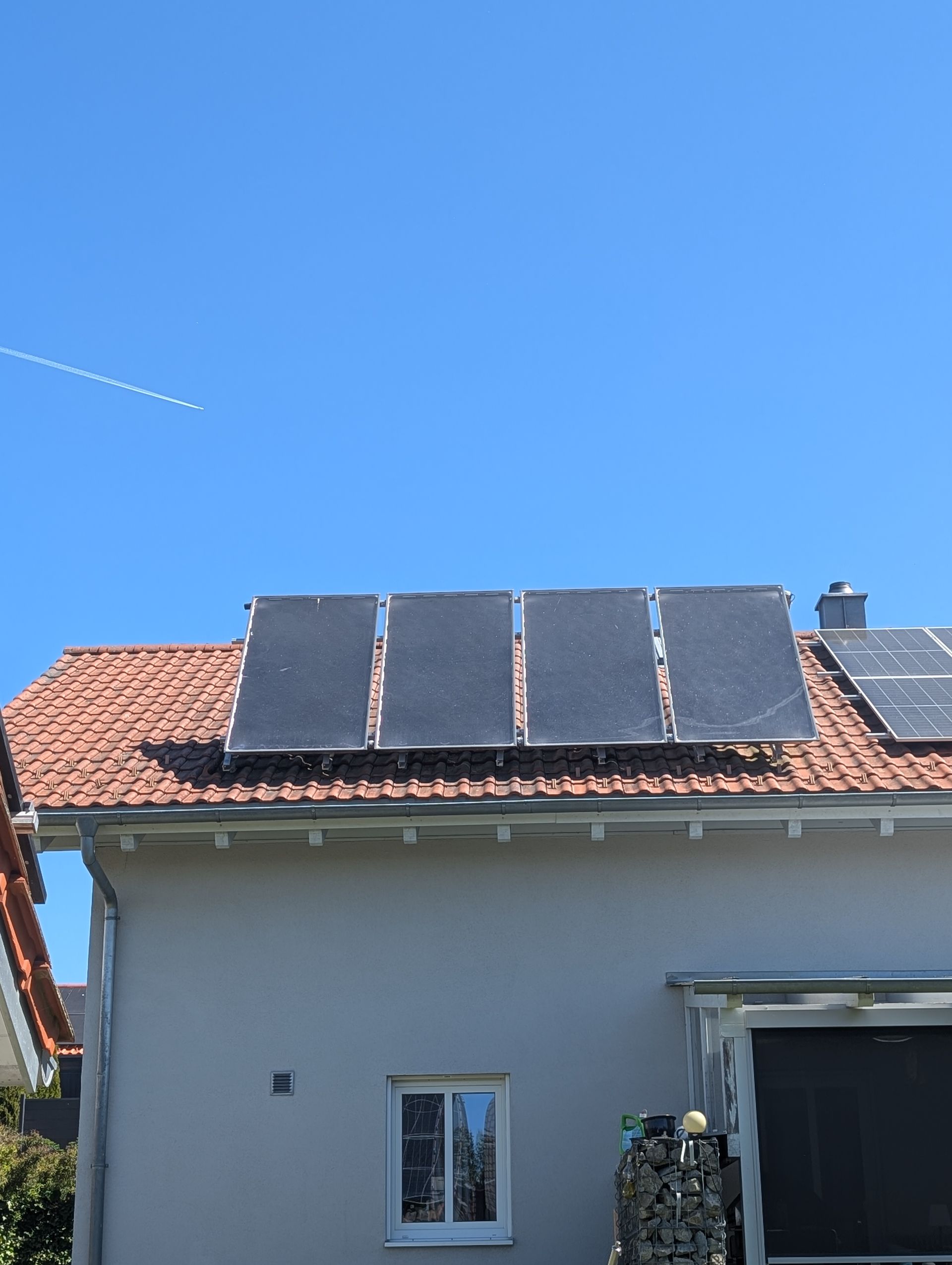 Zwei Arbeiter in Warnwesten gehen bei Sonnenuntergang über eine große Solaranlage auf einem Dach.