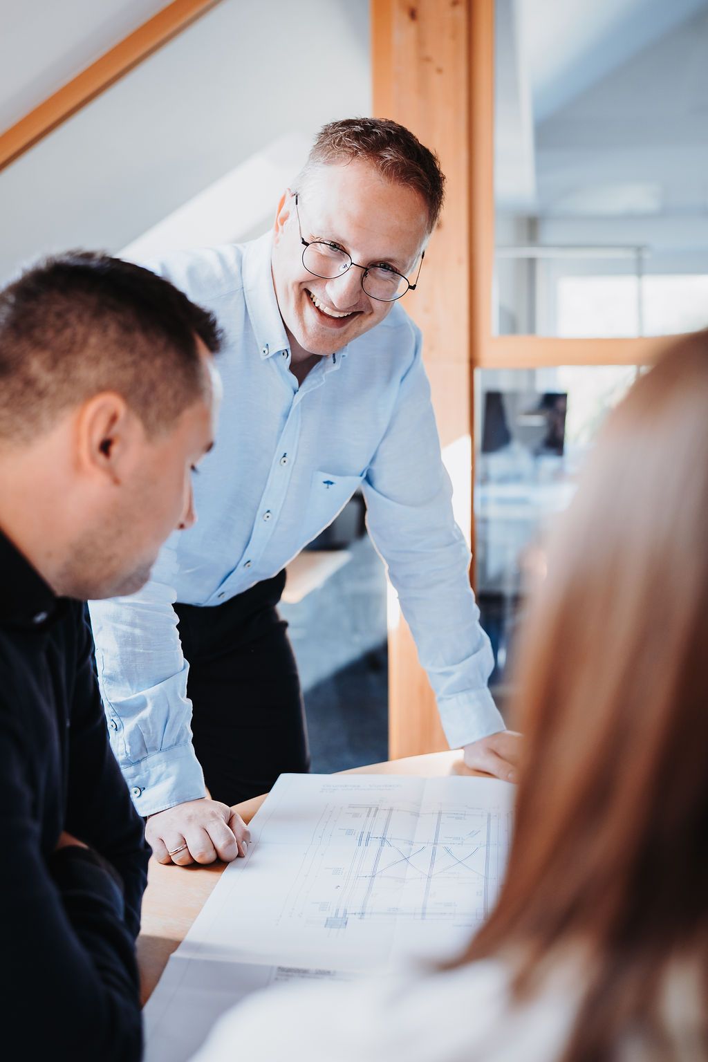 Eine Gruppe von Menschen sitzt um einen Tisch herum und betrachtet einen Bauplan.