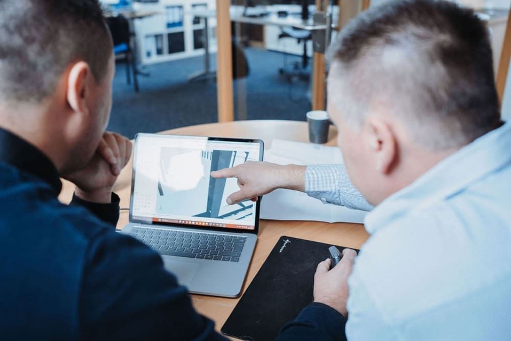 Zwei Männer sitzen an einem Tisch und schauen auf einen Laptop.