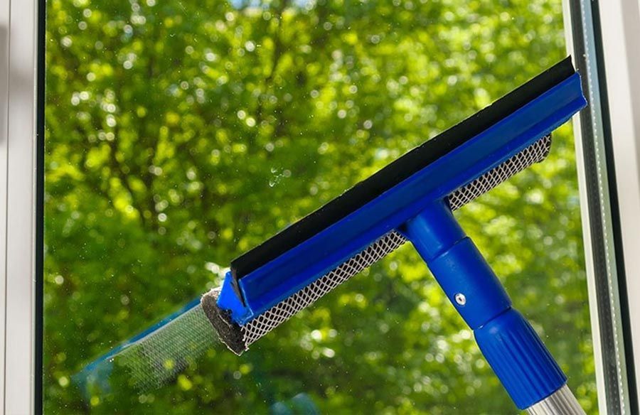 Una escobilla de goma azul está limpiando una ventana con árboles al fondo.