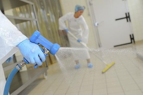 Una persona está rociando agua sobre un piso de baldosas con una manguera.