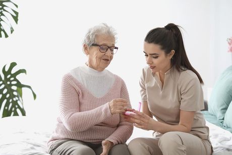 Una anciana está sentada en una cama con una enfermera.