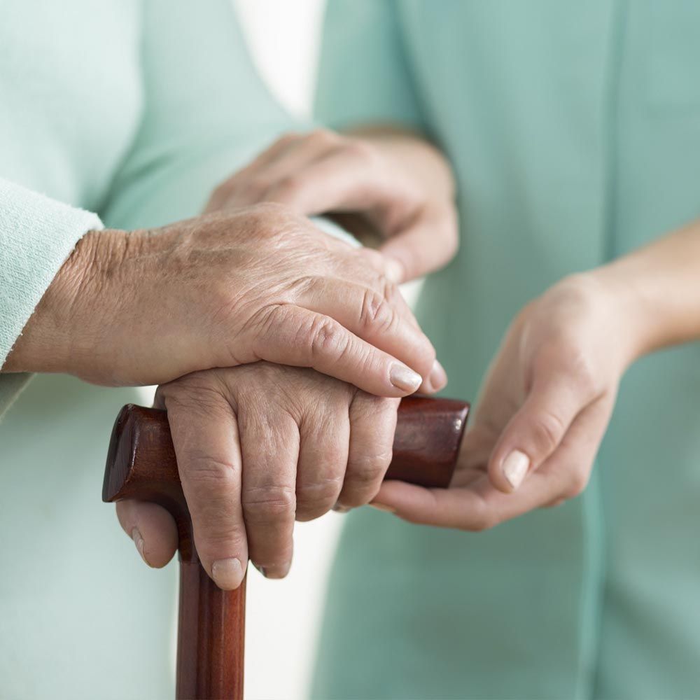 Una mujer sostiene la mano de una anciana mientras sostiene un bastón.