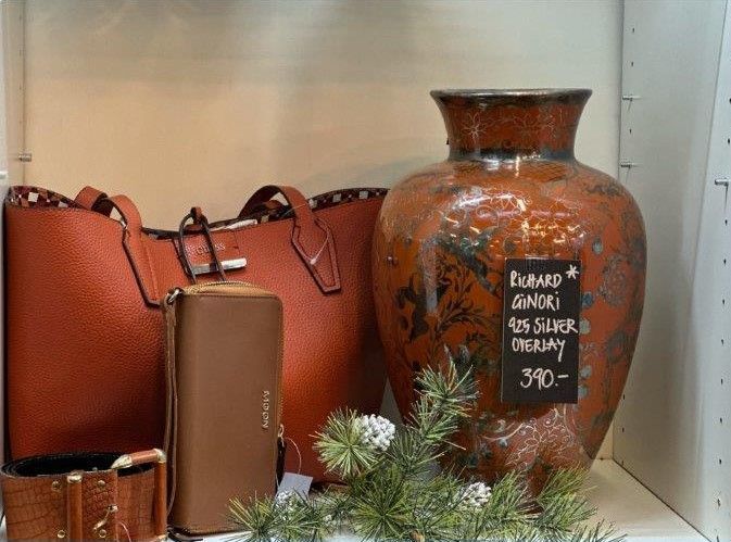 Eine braune Vase steht neben einer Handtasche auf einem Regal.