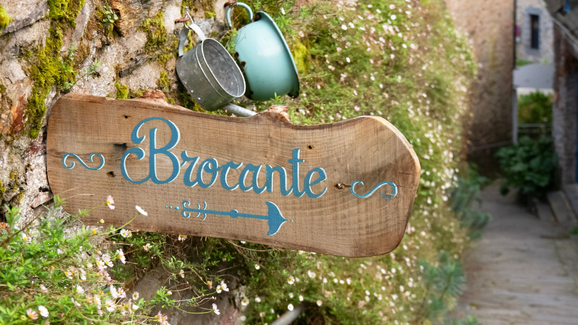 Panneau en bois avec le mot Brocante avec texte bleu sarcelle et flèche, accroché au mur avec des tasses.