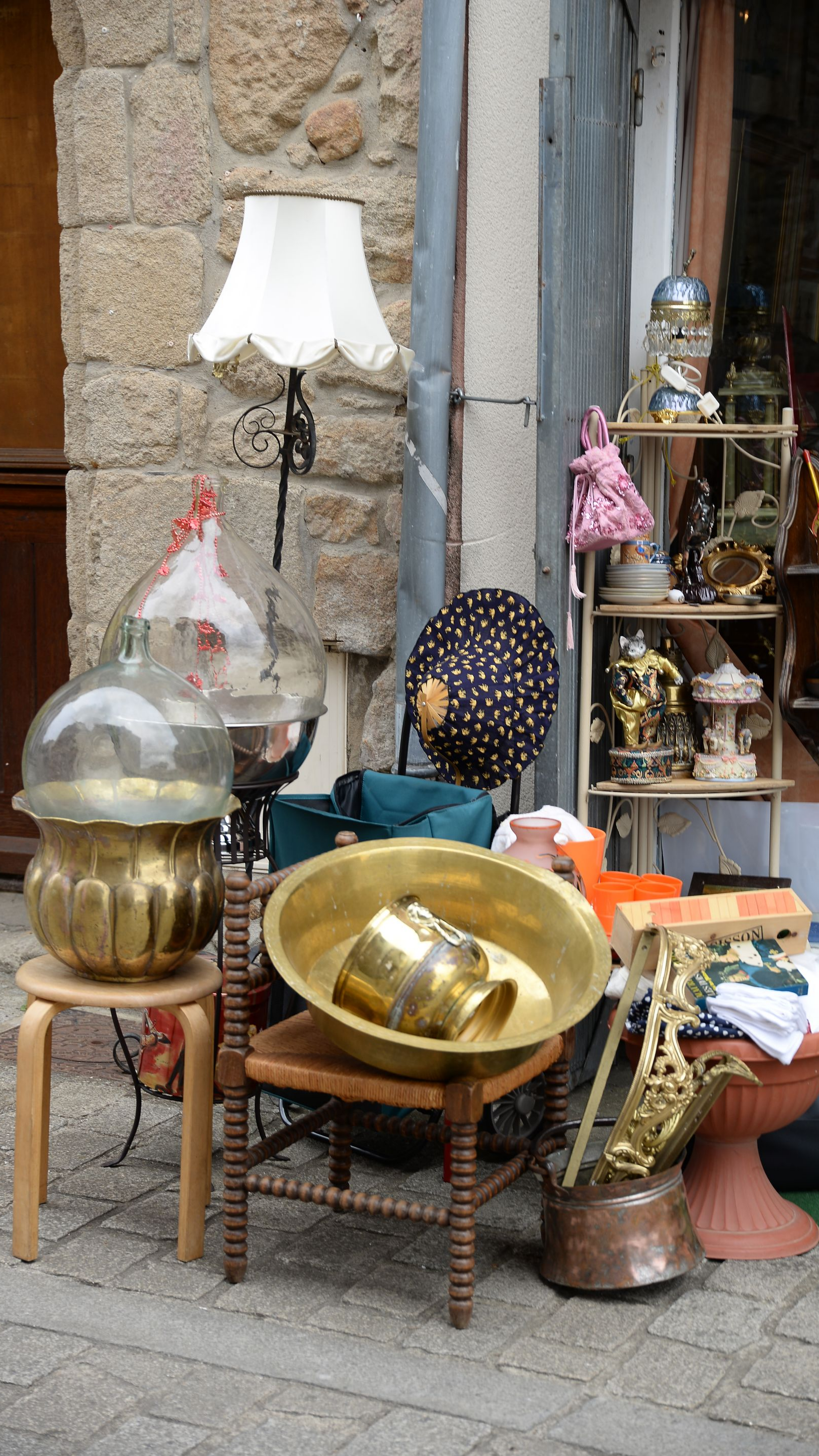 Objets anciens exposés à l'extérieur d'une boutique : lampes, bols, chapeaux et statues sur de petits tabourets et chaises.
