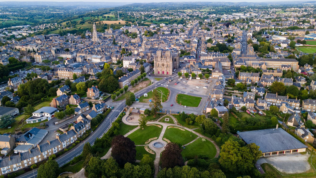 Vue aérienne d'une ville européenne avec une grande cathédrale et un parc, entourée de bâtiments et de verdure.