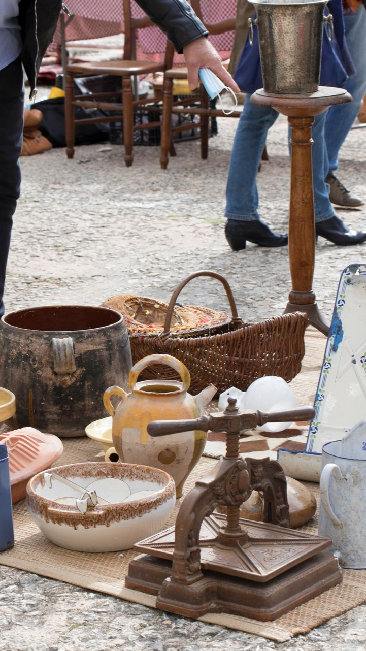 Une table avec divers objets vintage : poterie, panier, théière, support en métal et presse.