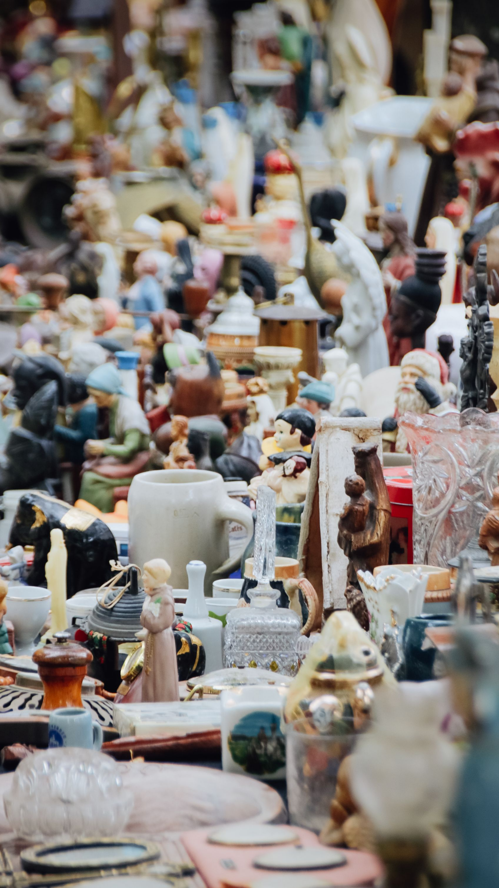 Un stand de marché aux puces bondé avec diverses figurines, vases et bibelots de différentes tailles et couleurs.