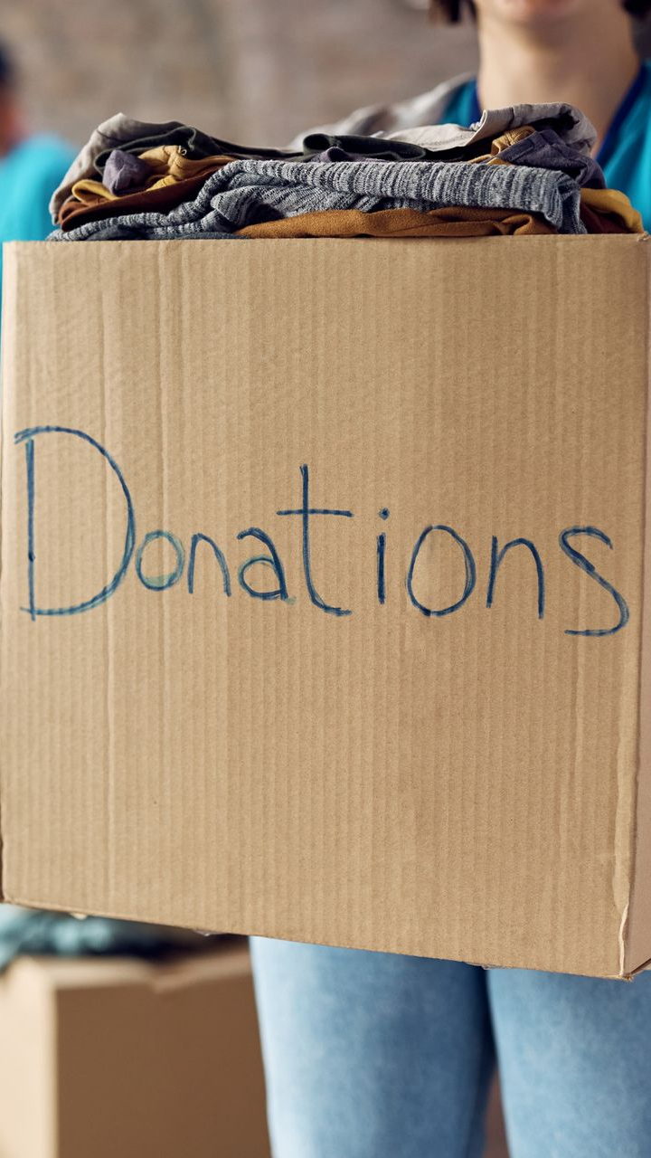 Une personne tenant une boîte en carton étiquetée du mot Donations, remplie de vêtements.