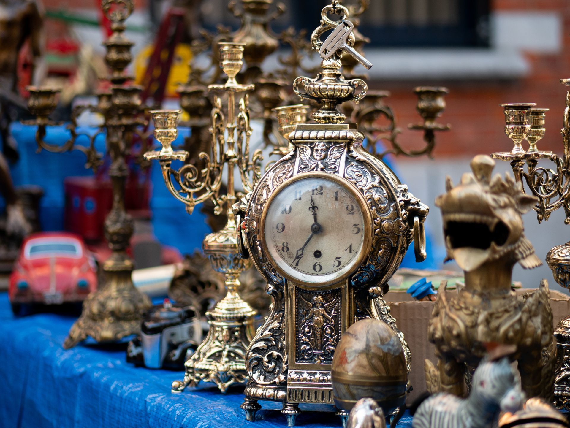 Objets anciens exposés sur une nappe bleue, notamment des horloges ornées, des chandeliers et des petits jouets.
