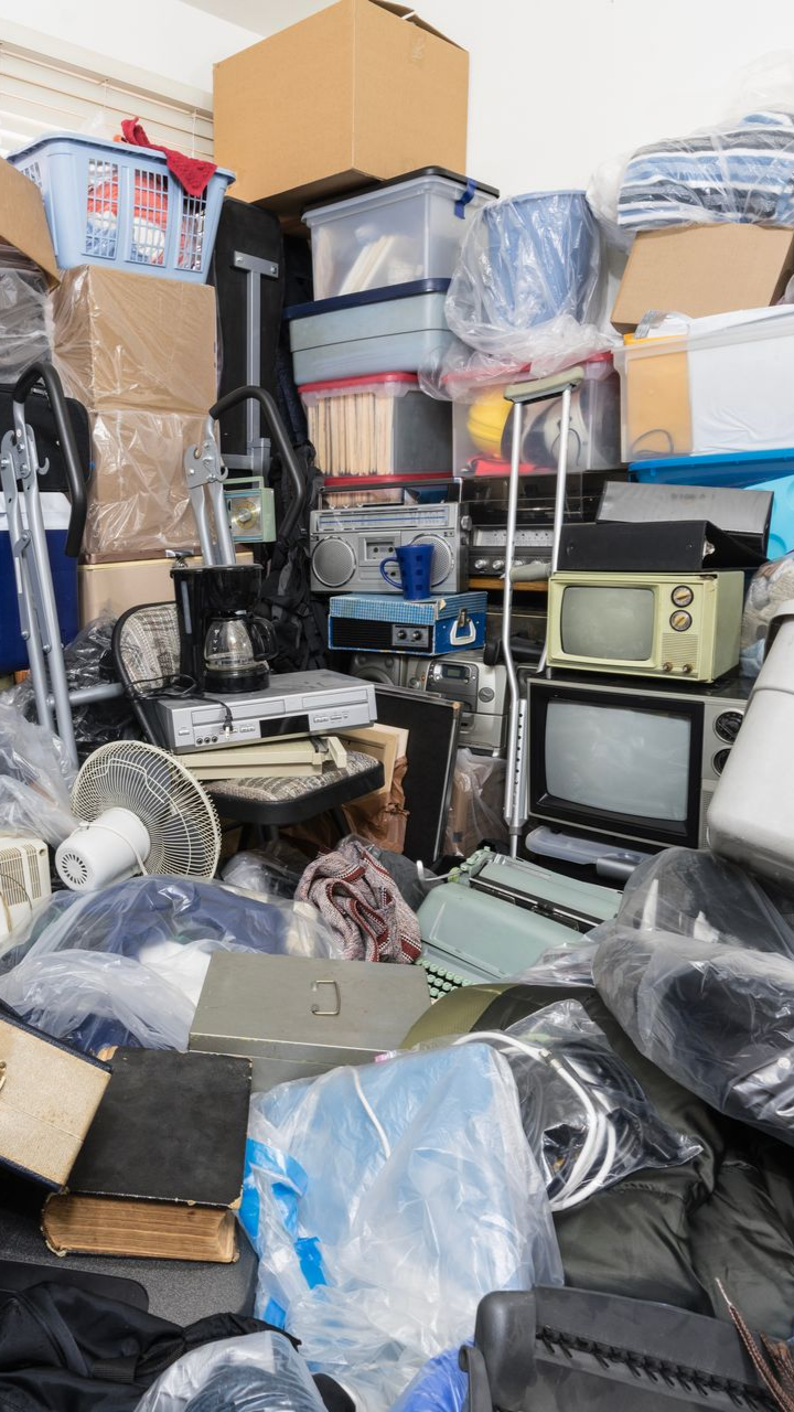 Chambre d'une maison de collectionneur remplie de sacs à vêtements, d'objets ménagers, d'appareils électroniques vintage et de déchets divers.