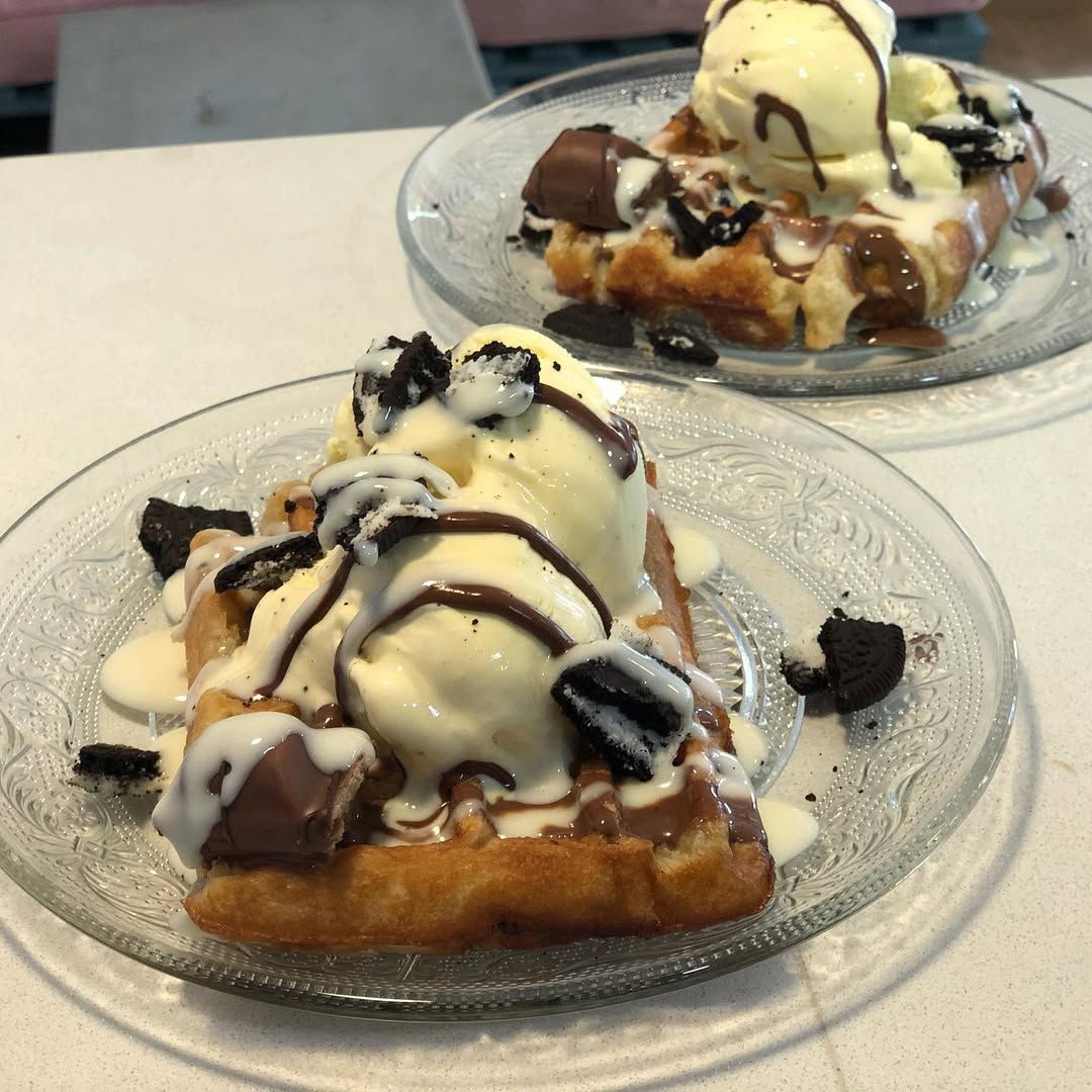 Dos gofres servidos en platos de cristal, cubiertos con bolas de helado de vainilla
