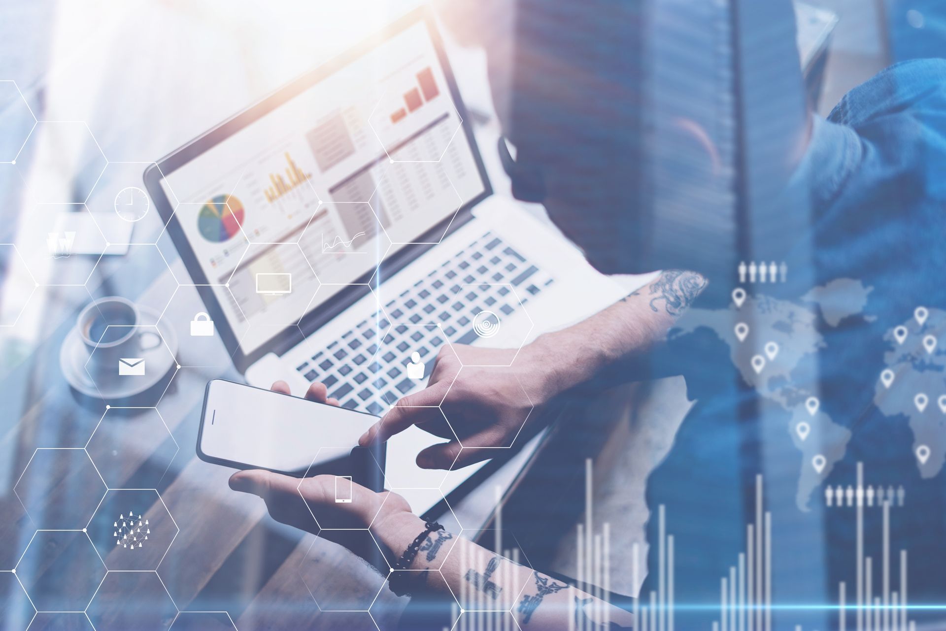 Un hombre está sentado en una mesa usando una computadora portátil y un teléfono celular.