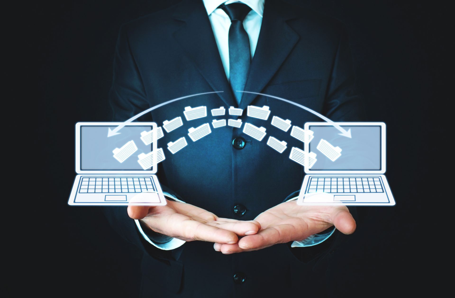 Un hombre con traje y corbata sostiene dos computadoras portátiles en sus manos.