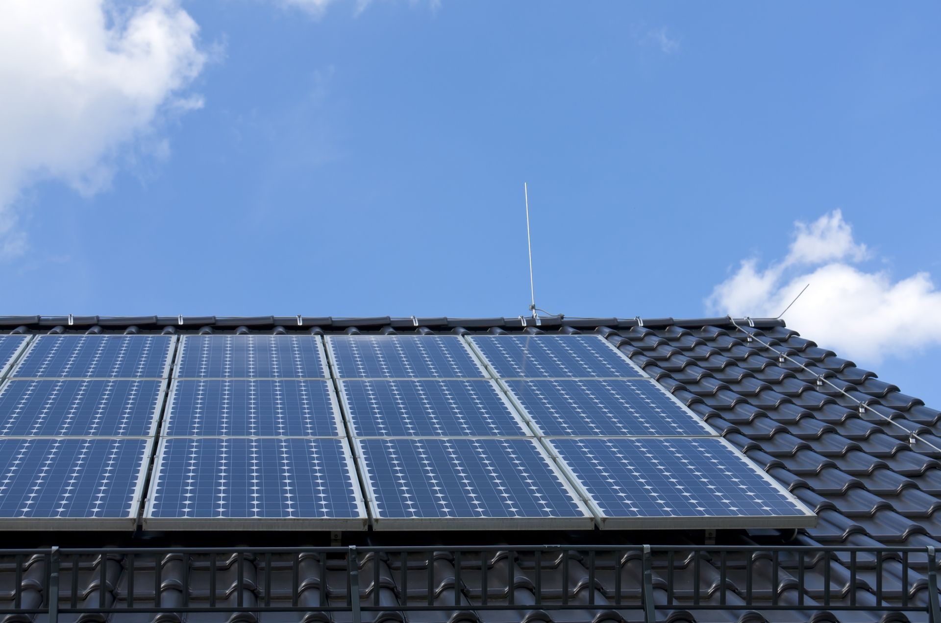 Nahaufnahme von dunklen Solarzellen, die auf einer Holzkonstruktion unter einem strahlend blauen Himmel mit leichten, zarten Wolken montiert sind.