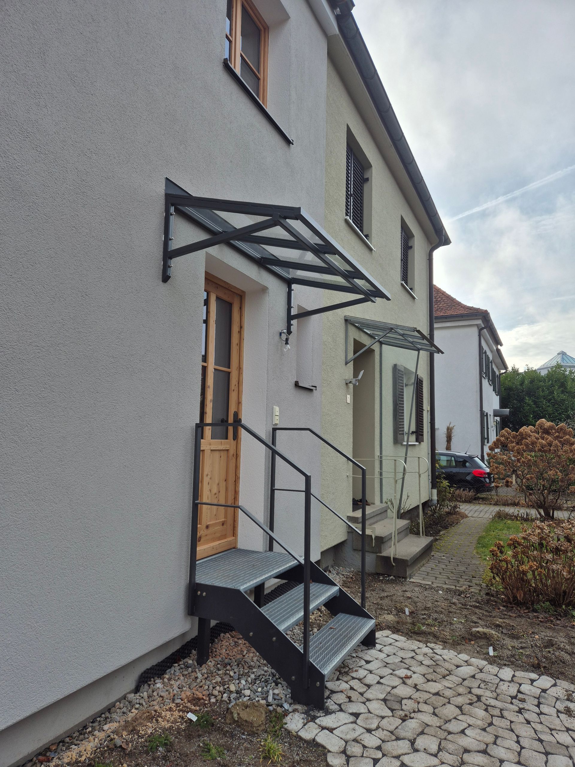 Ein angeschrägtes Metallvordach mit Glas an einer hellen Hauswand