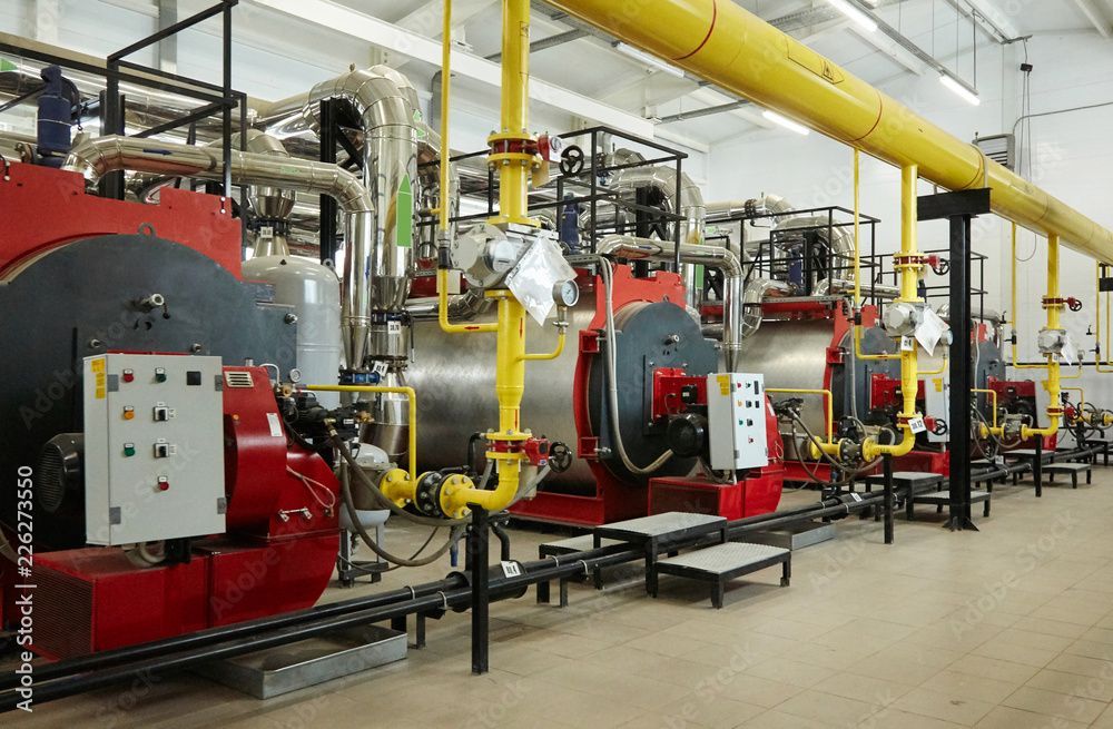 Chaufferie industrielle avec chaudières rouges, tuyaux jaunes et panneaux de commande dans un environnement d'usine