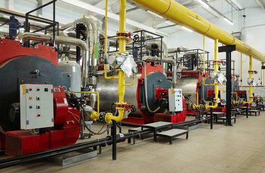 Chaufferie industrielle avec chaudières rouges, tuyaux jaunes et panneaux de commande dans un environnement d'usine