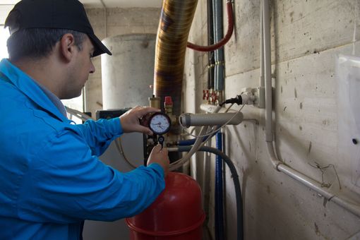 Ouvrier en veste bleue vérifiant un manomètre sur un réservoir rouge dans une salle des machines en béton