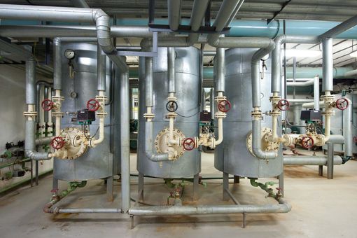 Tuyaux et vannes industriels dans une salle des machines avec de grands réservoirs métalliques et des conduits de ventilation