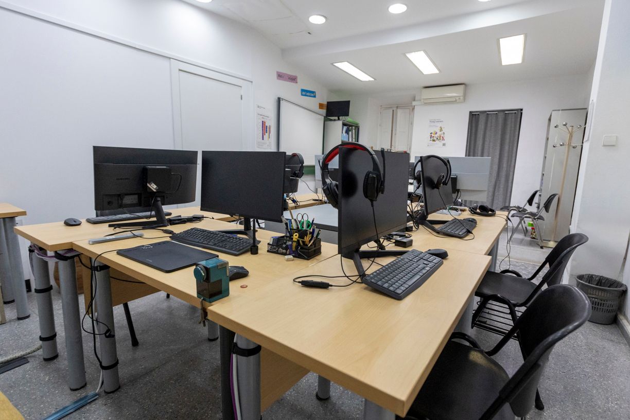 Espacio de trabajo de oficina con varias computadoras, teclados, auriculares y sillas.