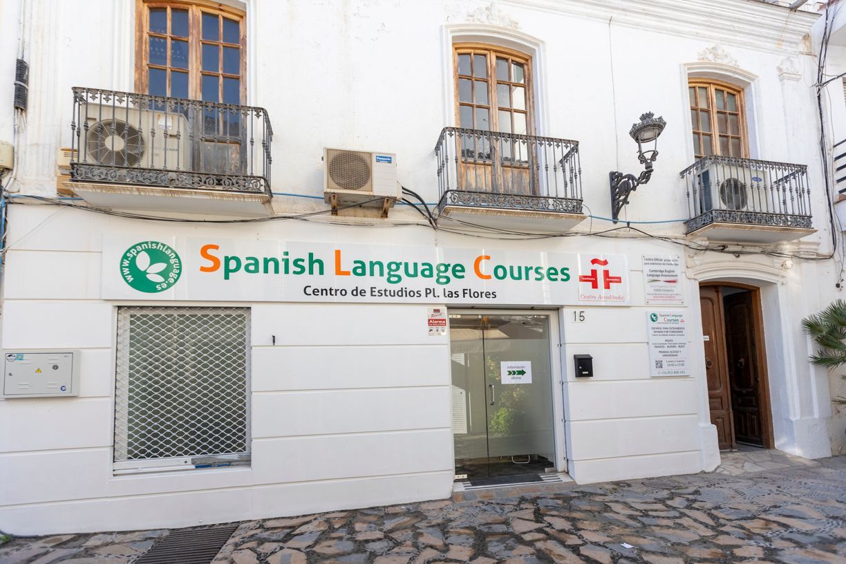 Exterior de una escuela de español con fachada blanca y cartel verde.