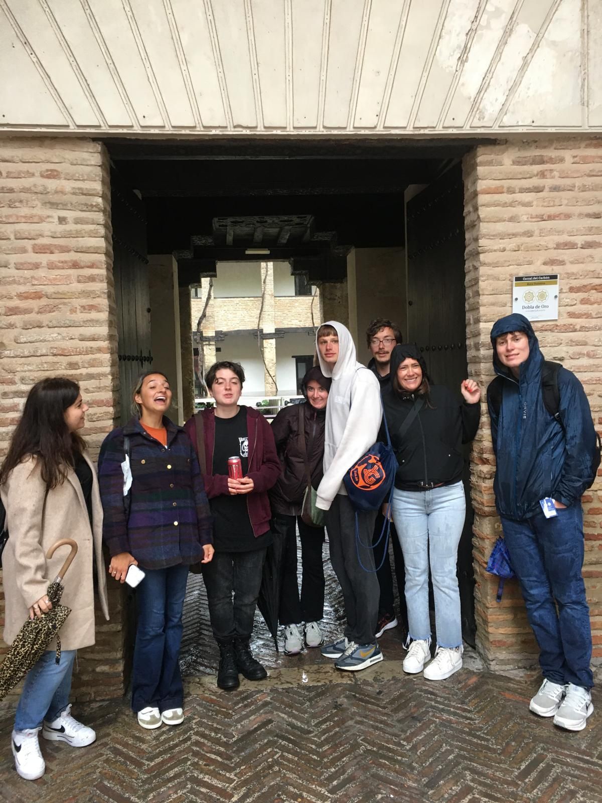 Grupo de estudiantes de pie bajo un arco de ladrillo. Algunos sonriendo. Al aire libre.