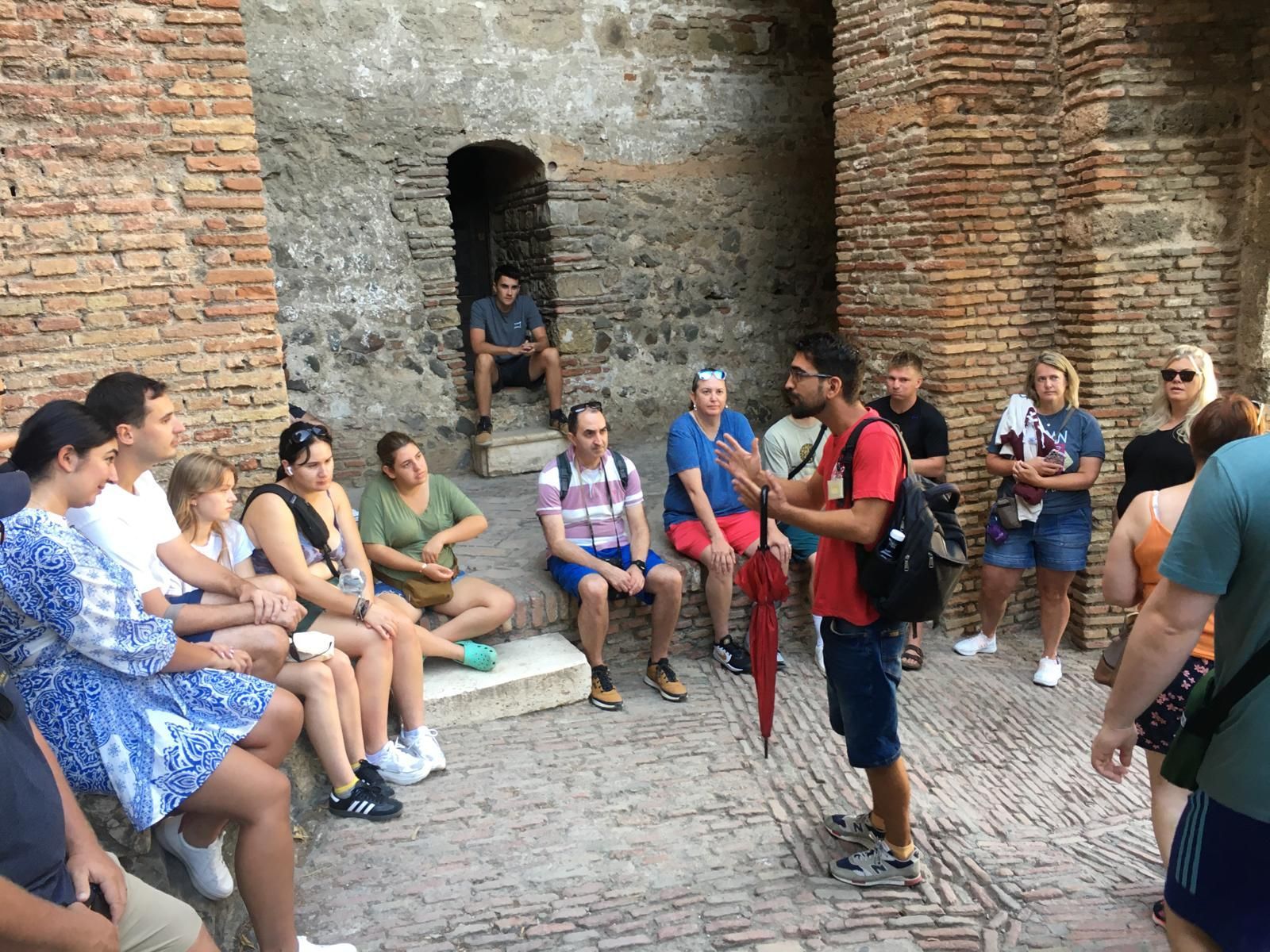 Un guía turístico con paraguas habla con un grupo en una antigua estructura de ladrillo.