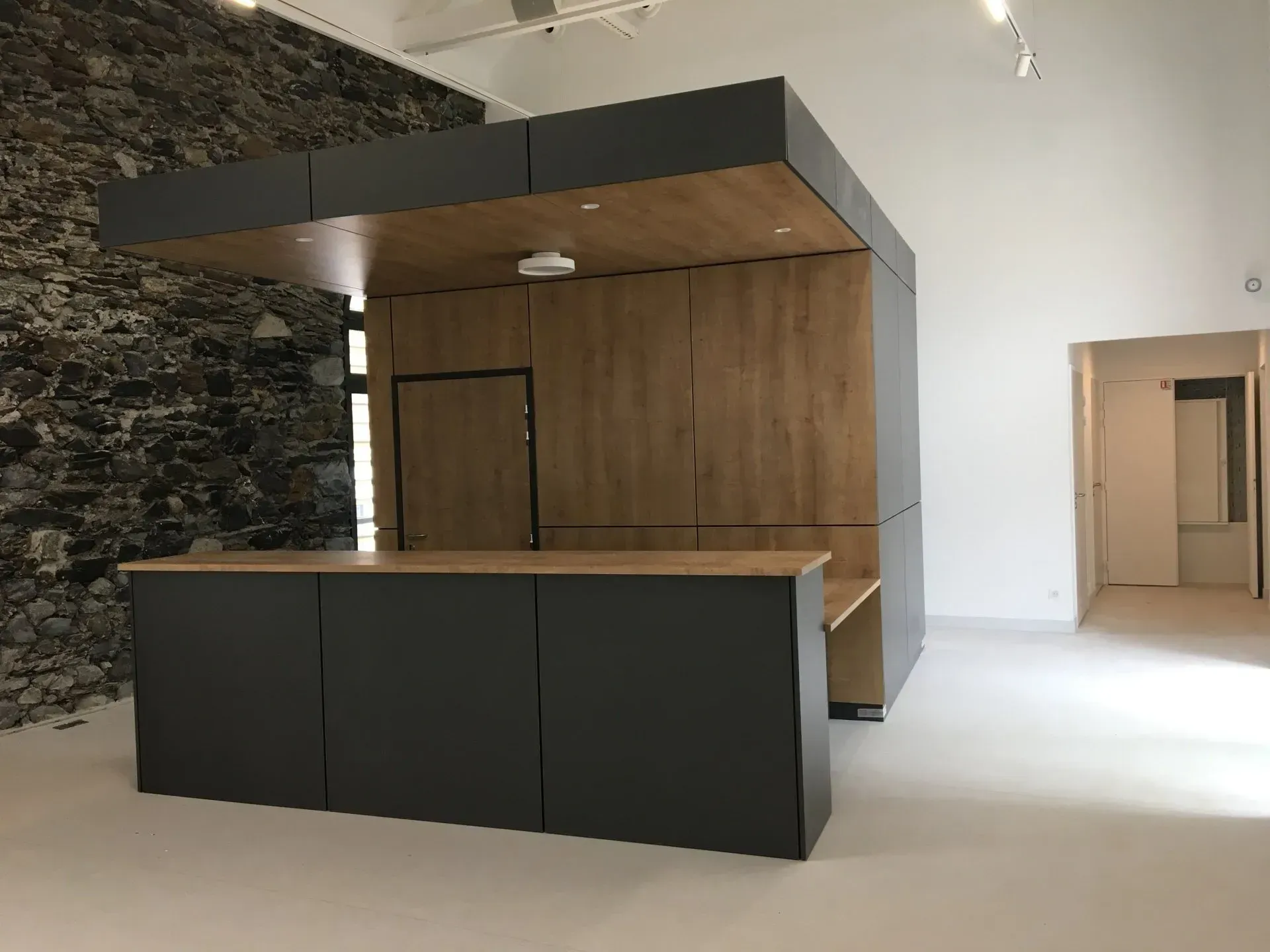 Îlot de cuisine moderne avec armoires gris foncé, comptoirs en bois clair et réfrigérateur intégré.