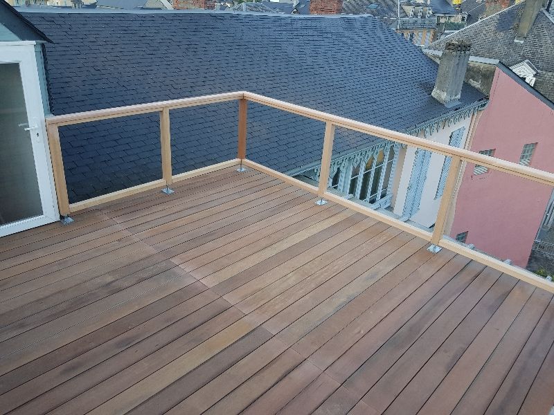 Terrasse en bois avec mobilier extérieur, bordée de rochers et faisant face à une maison moderne.