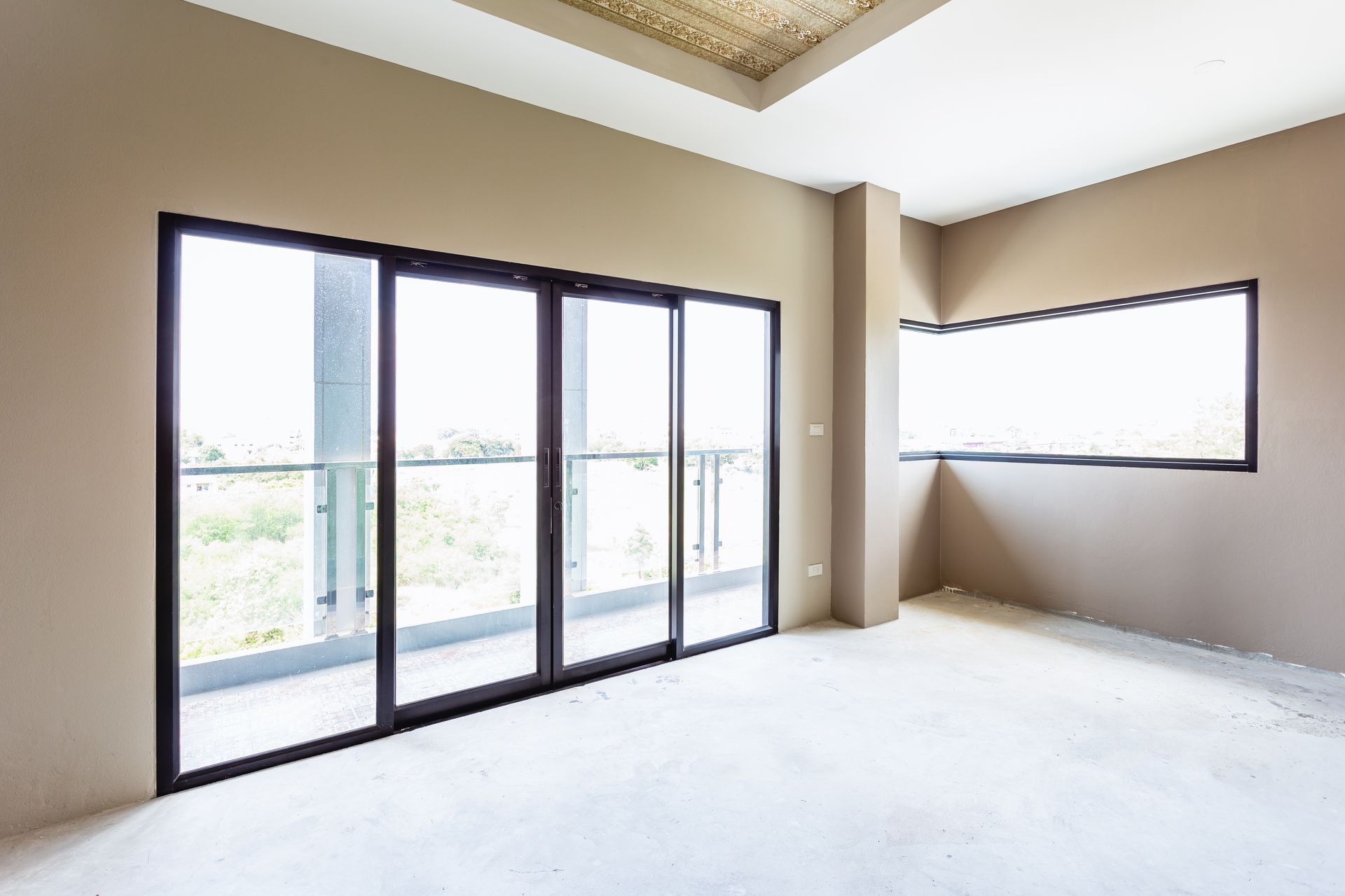 Pièce vide avec de grandes portes coulissantes en verre et une petite fenêtre. Murs marron clair, sol en béton.