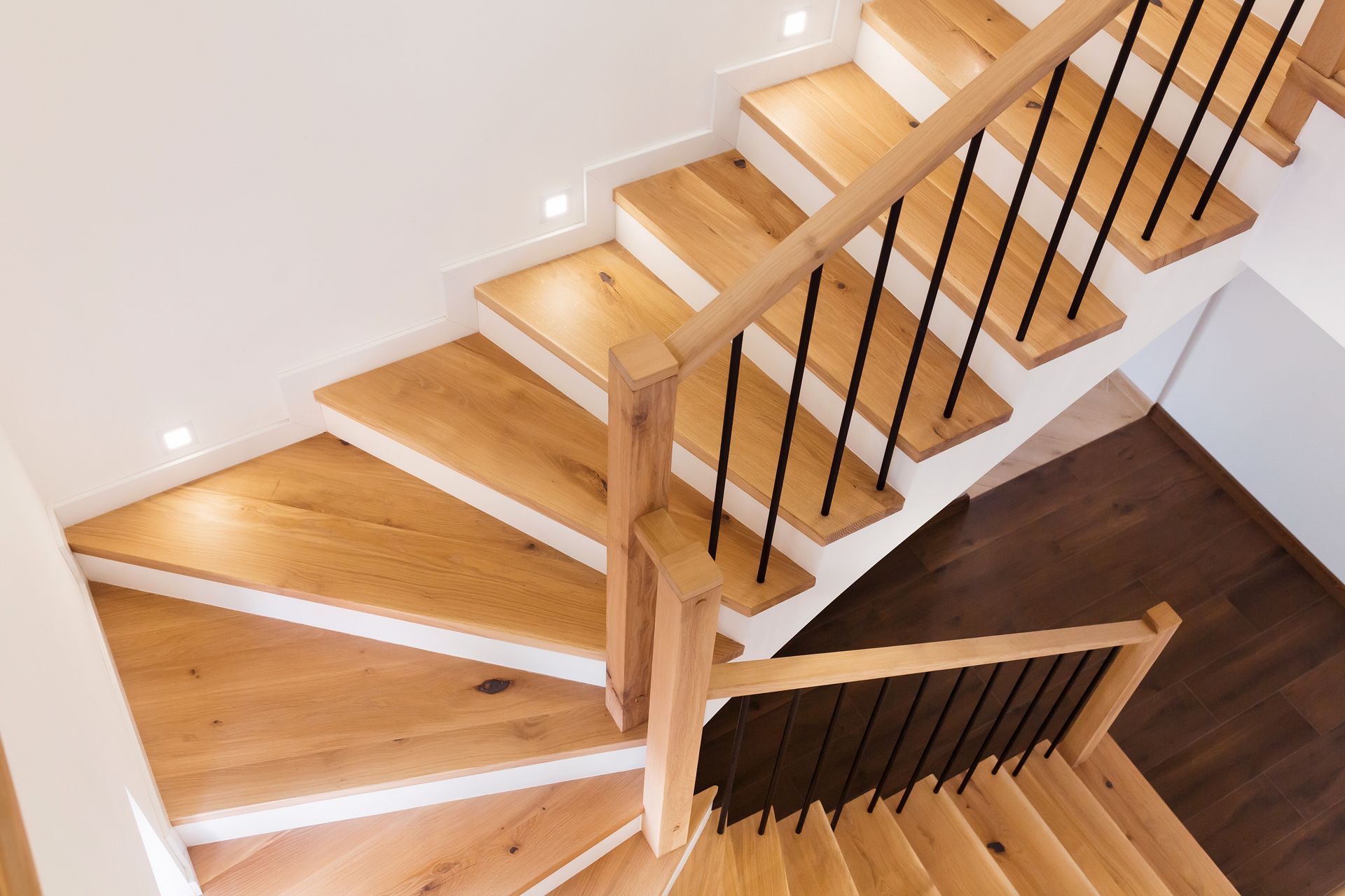 Escalier en bois avec rampes noires, accents blancs et éclairage encastré.