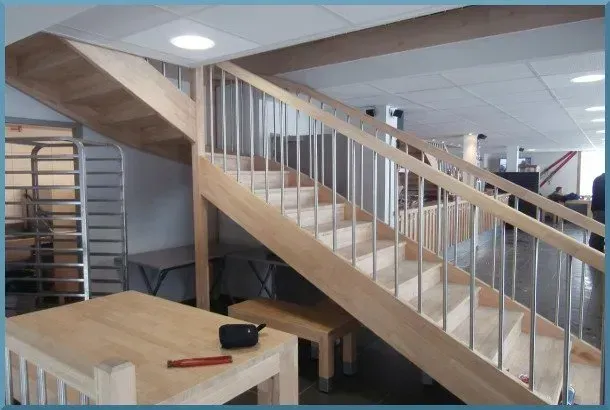Escalier en bois avec rampe en métal dans une pièce au plafond et aux murs de couleur claire.