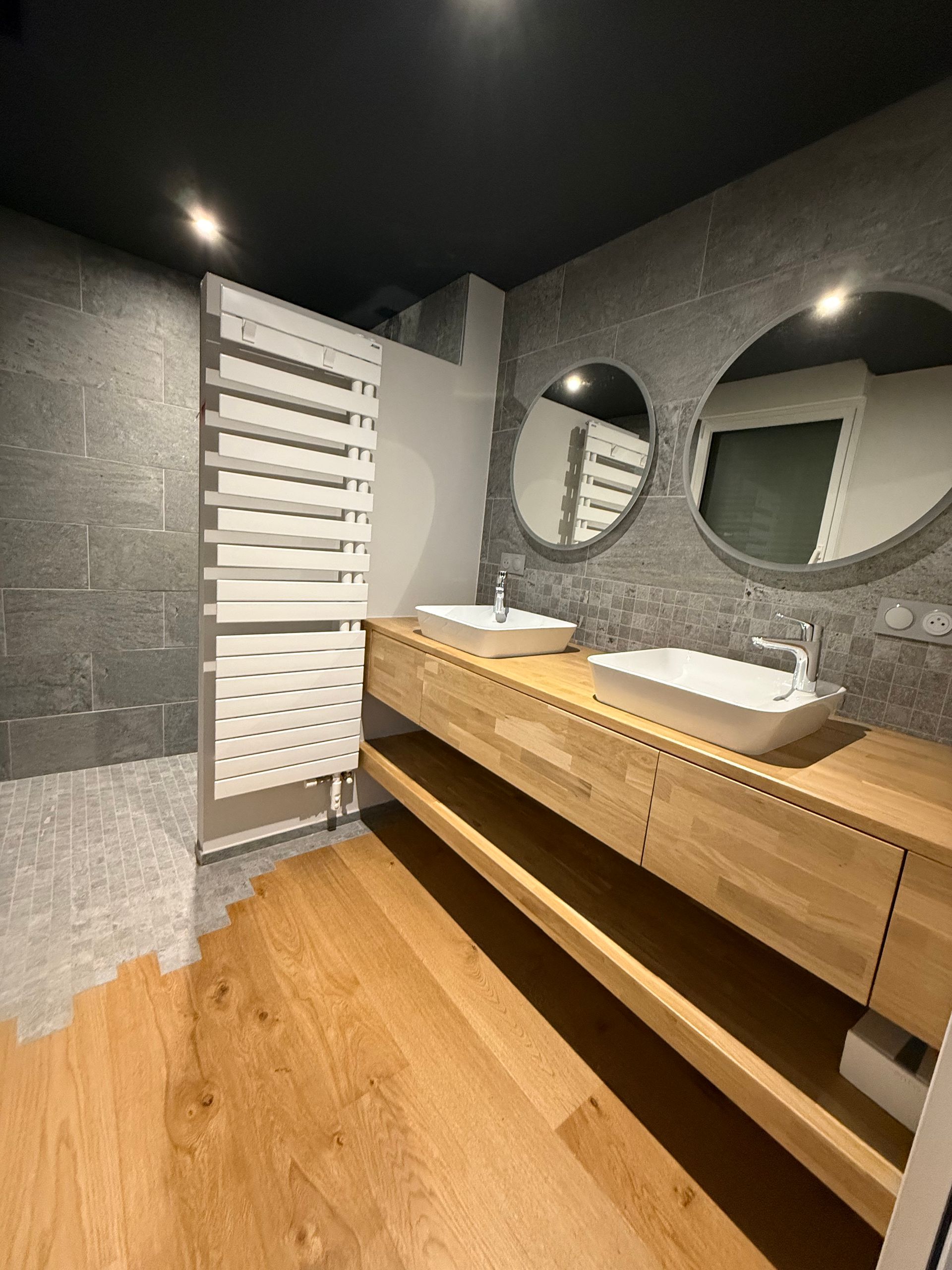 Îlot de cuisine moderne avec armoires gris foncé, comptoirs en bois clair et réfrigérateur intégré.