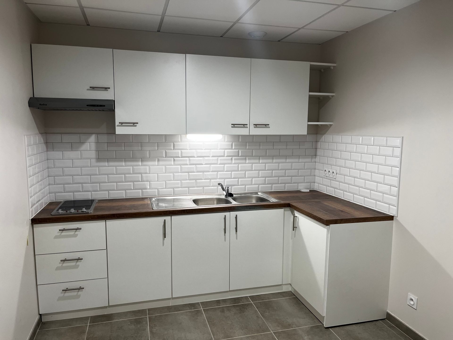 Cuisine moderne blanche en forme de U avec comptoirs en bois, appareils électroménagers en acier inoxydable et mur de verre à cadre noir.