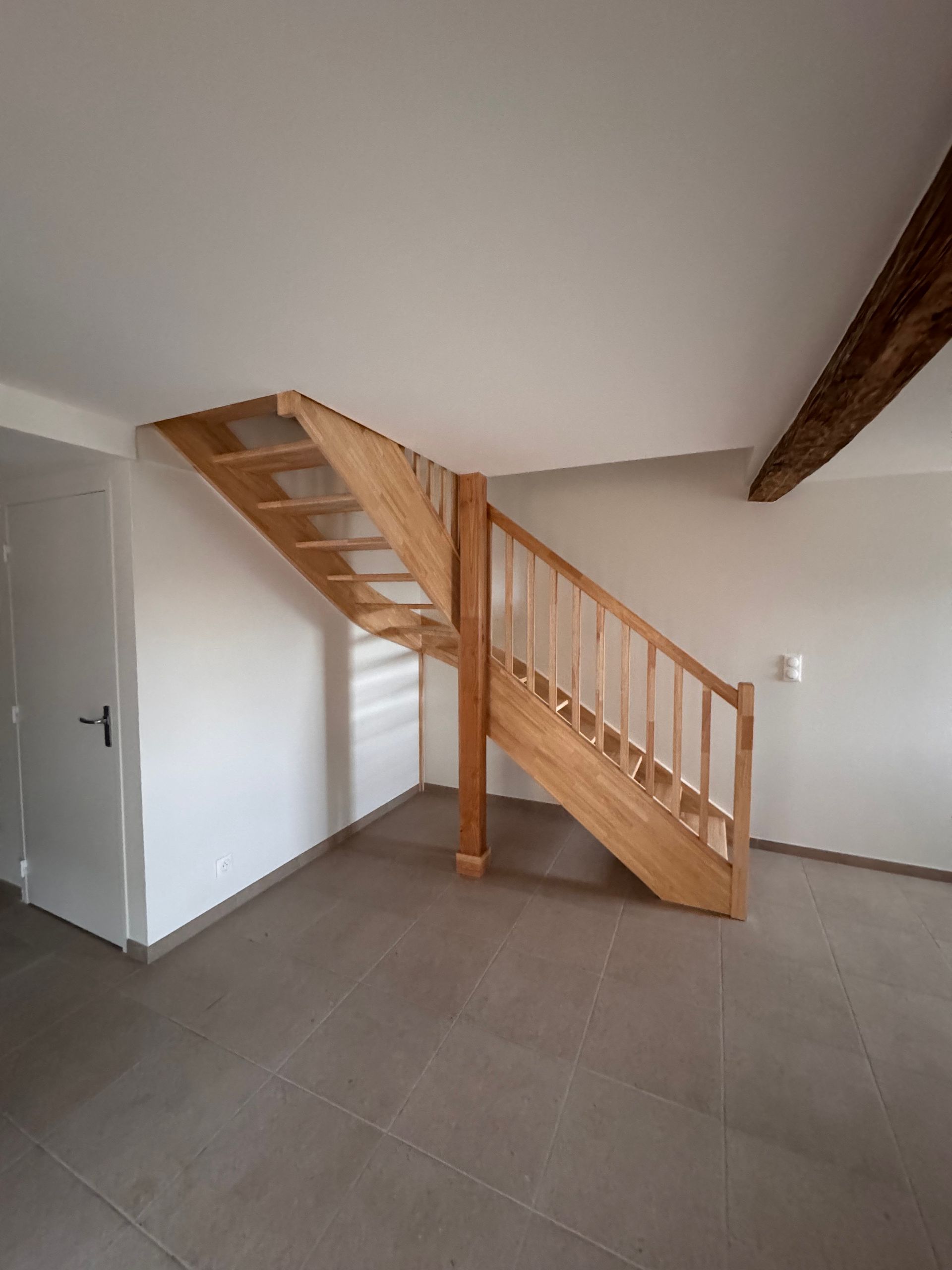Escalier avec rampes en bois et table blanche avec chaises dans une pièce de couleur neutre.