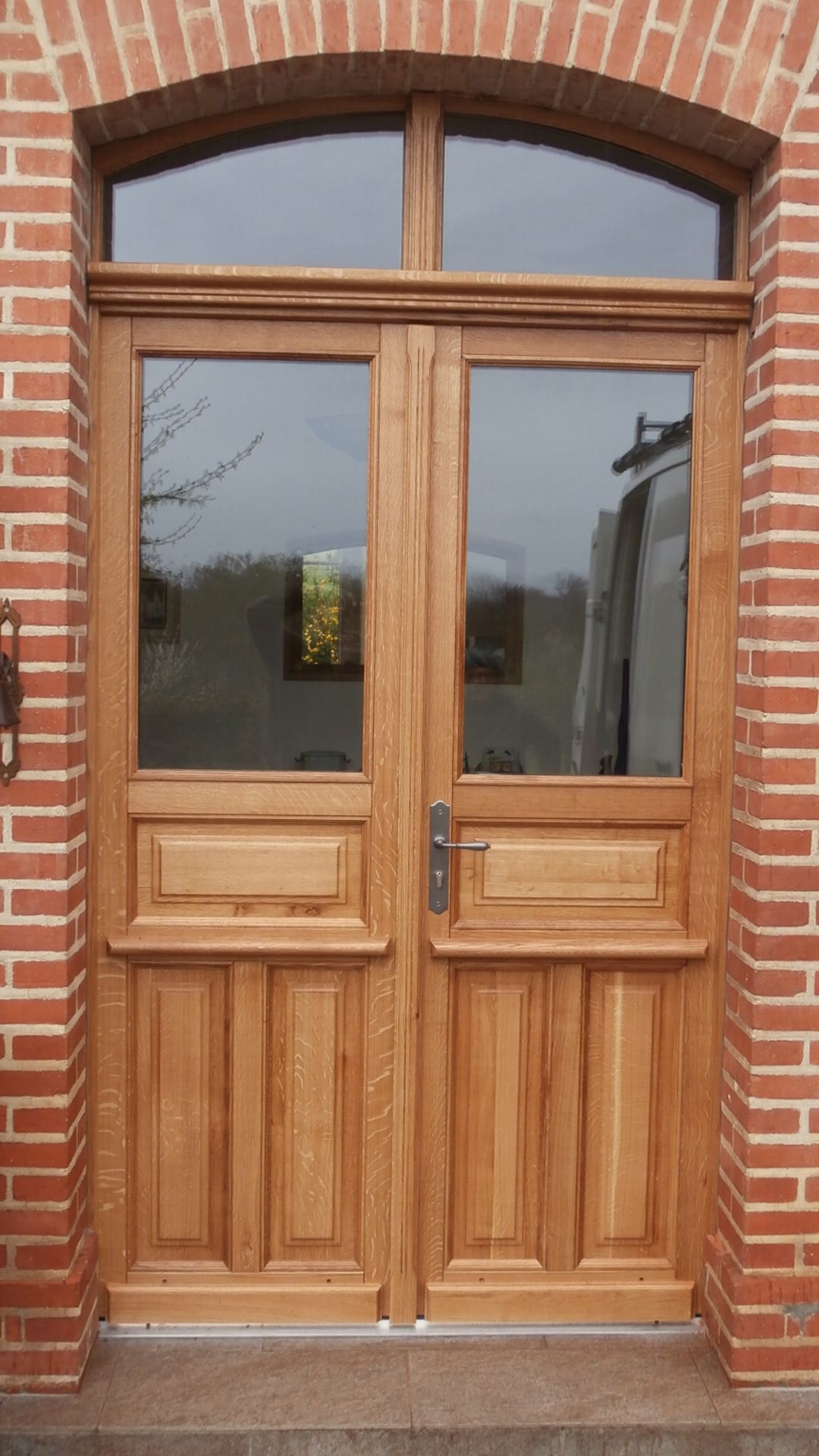 Porte d'entrée gris foncé aux accents carrés, flanquée de panneaux de verre, boîte aux lettres noire, maison blanche.