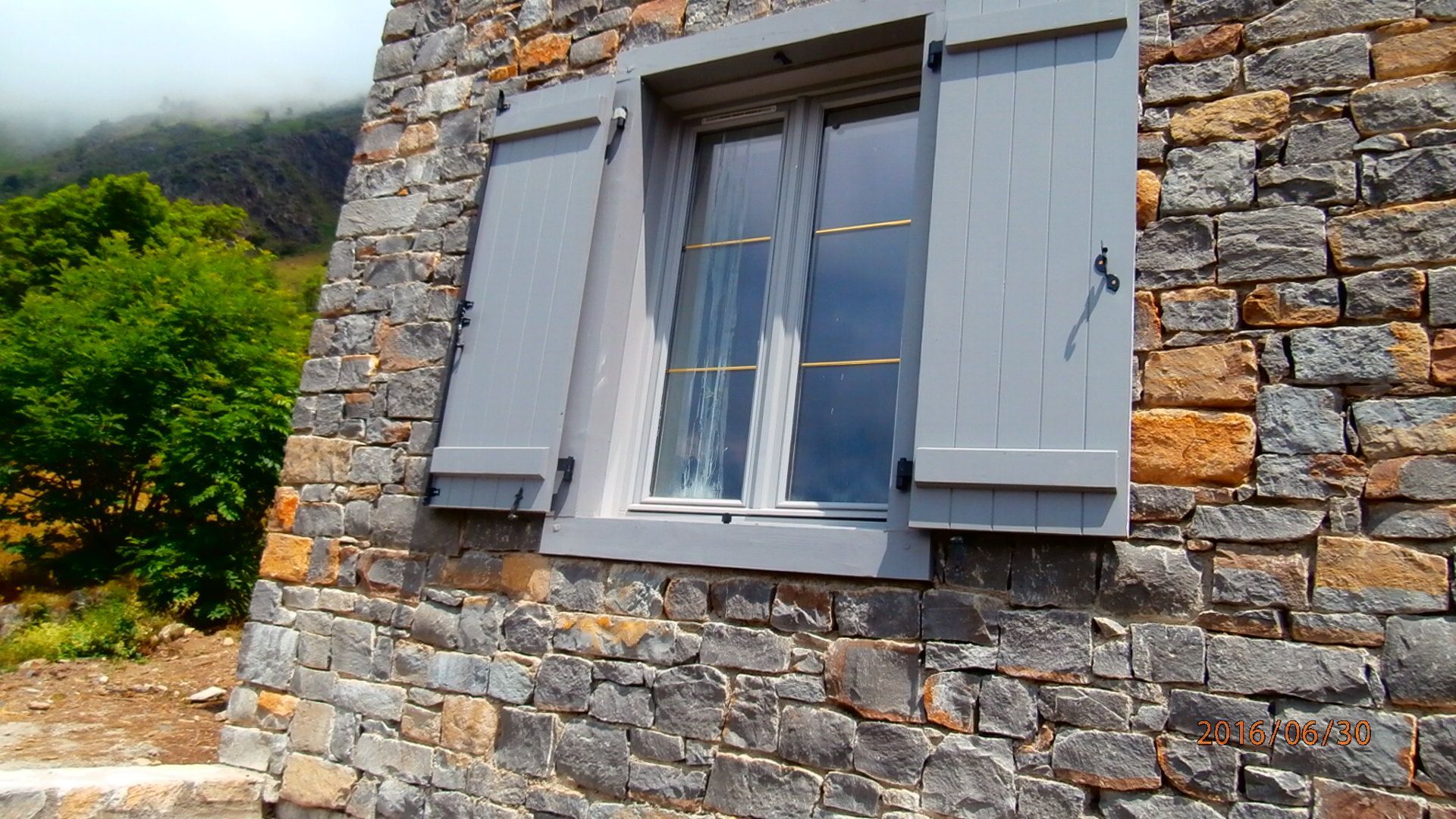 Fenêtre aux volets blancs ouverte sur un mur beige.