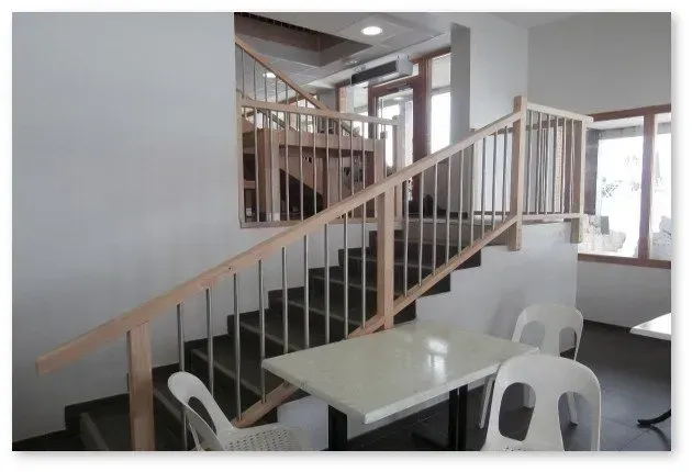 Escalier intérieur avec rampe en bois clair, escalier foncé et table avec chaises blanches.