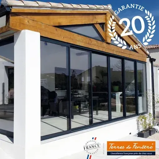 Véranda avec fenêtres à cadre noir, murs blancs et poutres en bois, mettant en valeur une étiquette « Made in France » et une garantie de 20 ans.