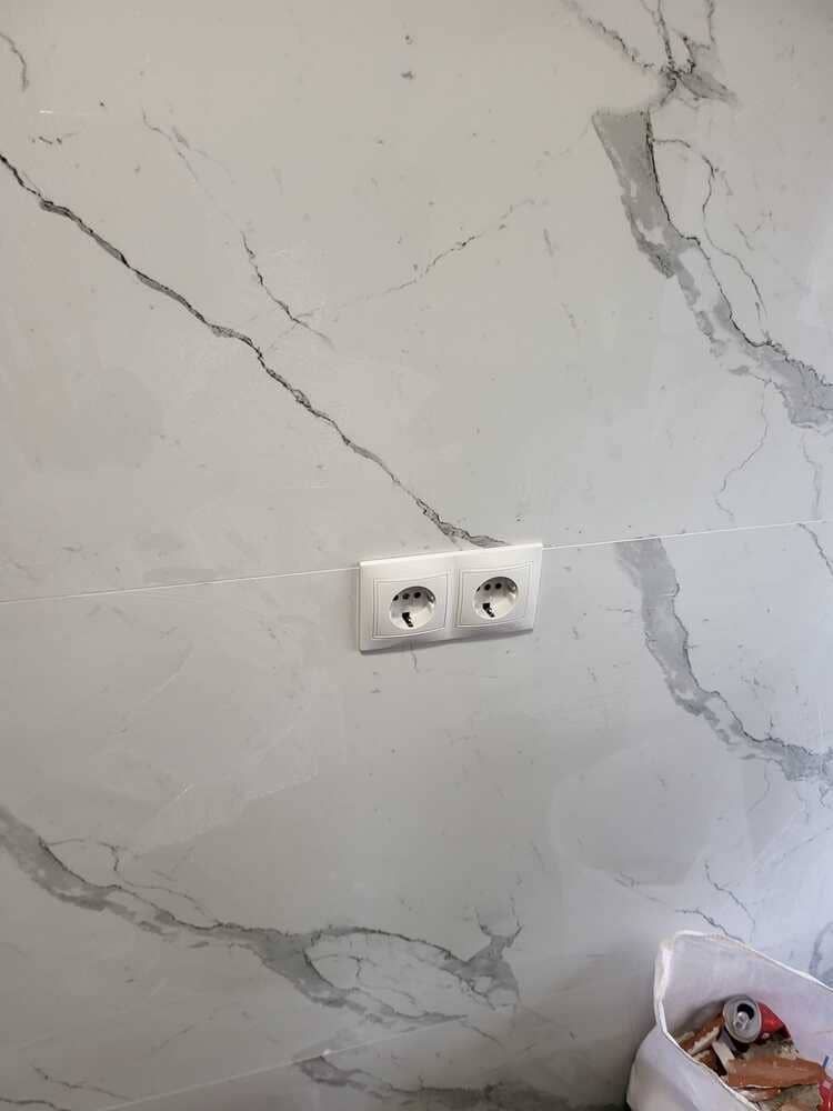 Pared de mármol blanco con dos enchufes eléctricos blancos.