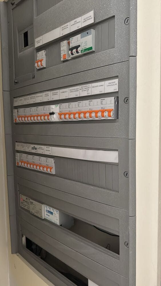 Panel eléctrico gris con disyuntores y etiquetas montados en una pared.