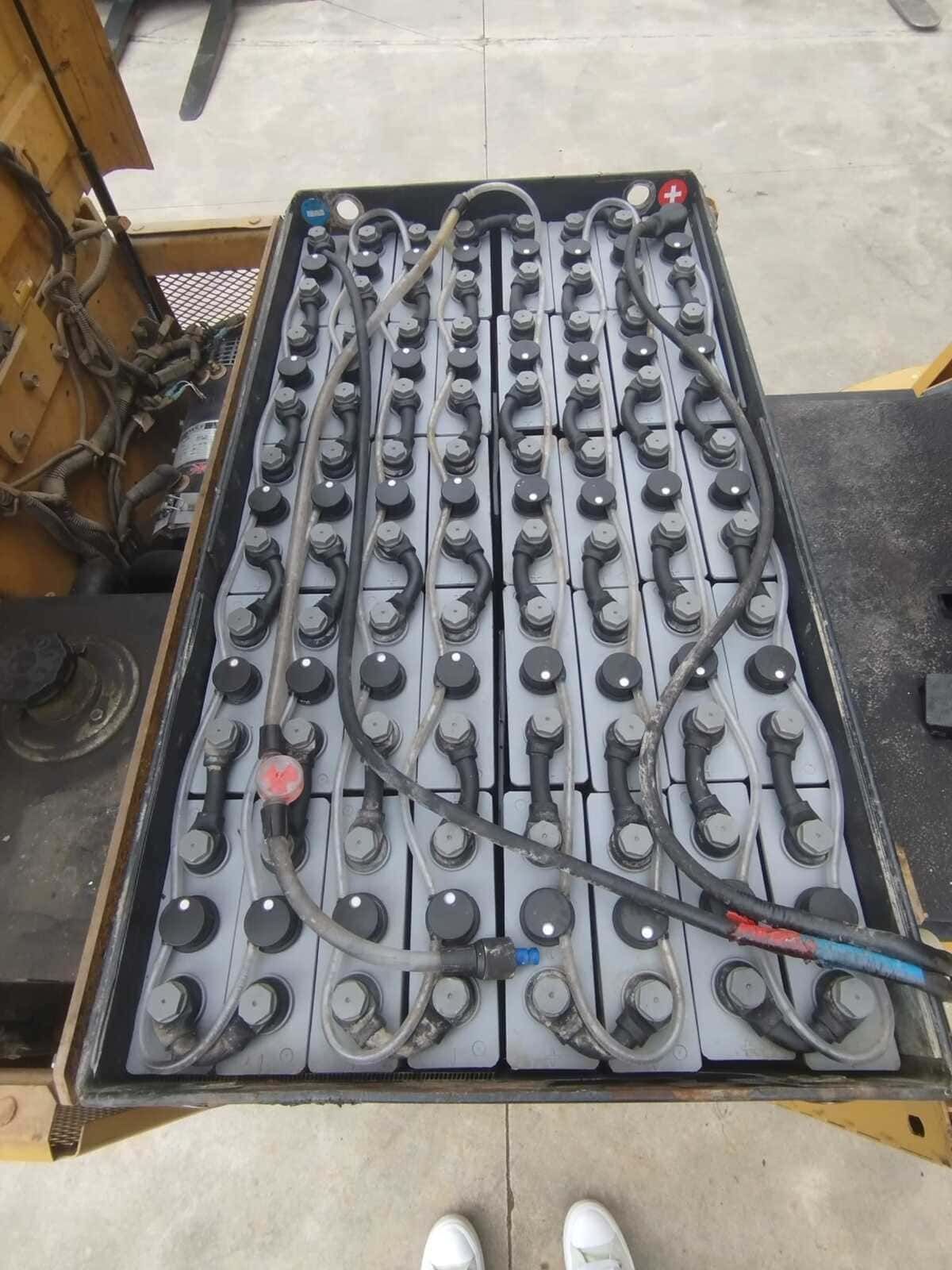 Una batería industrial de gran tamaño para montacargas, con múltiples celdas y cableado conectado, se encuentra dentro de una carcasa amarilla para vehículos.