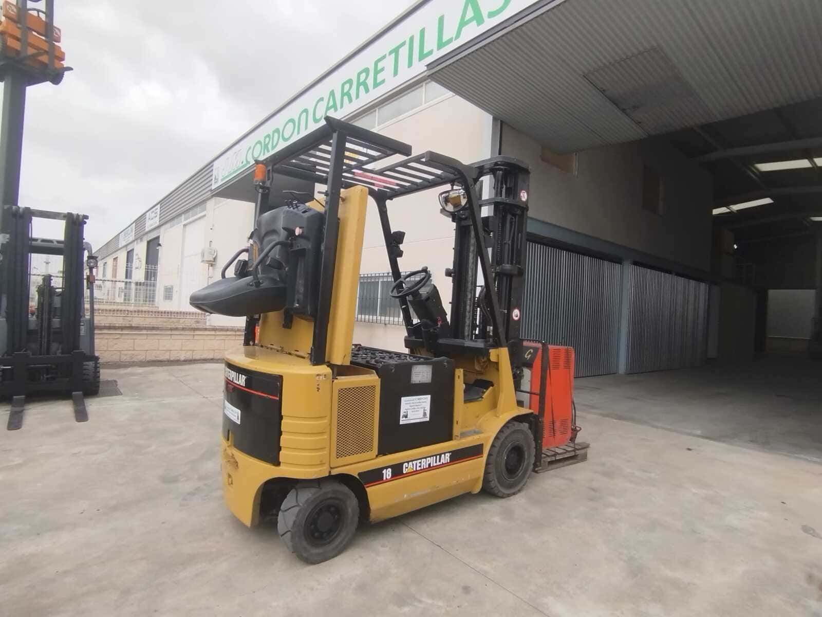 Una carretilla elevadora Caterpillar amarilla estacionada en un terreno de hormigón frente a un almacén.
