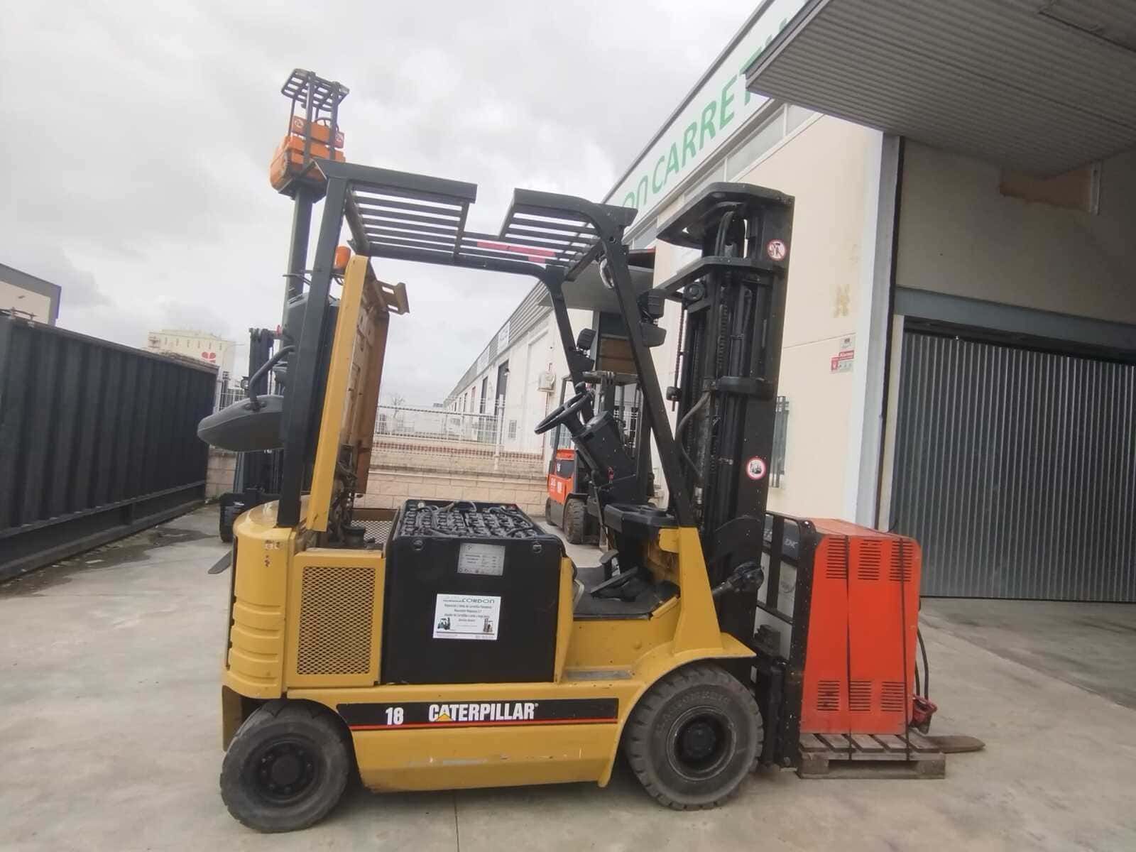 Una carretilla elevadora Caterpillar amarilla estacionada en un terreno de hormigón frente a un almacén.