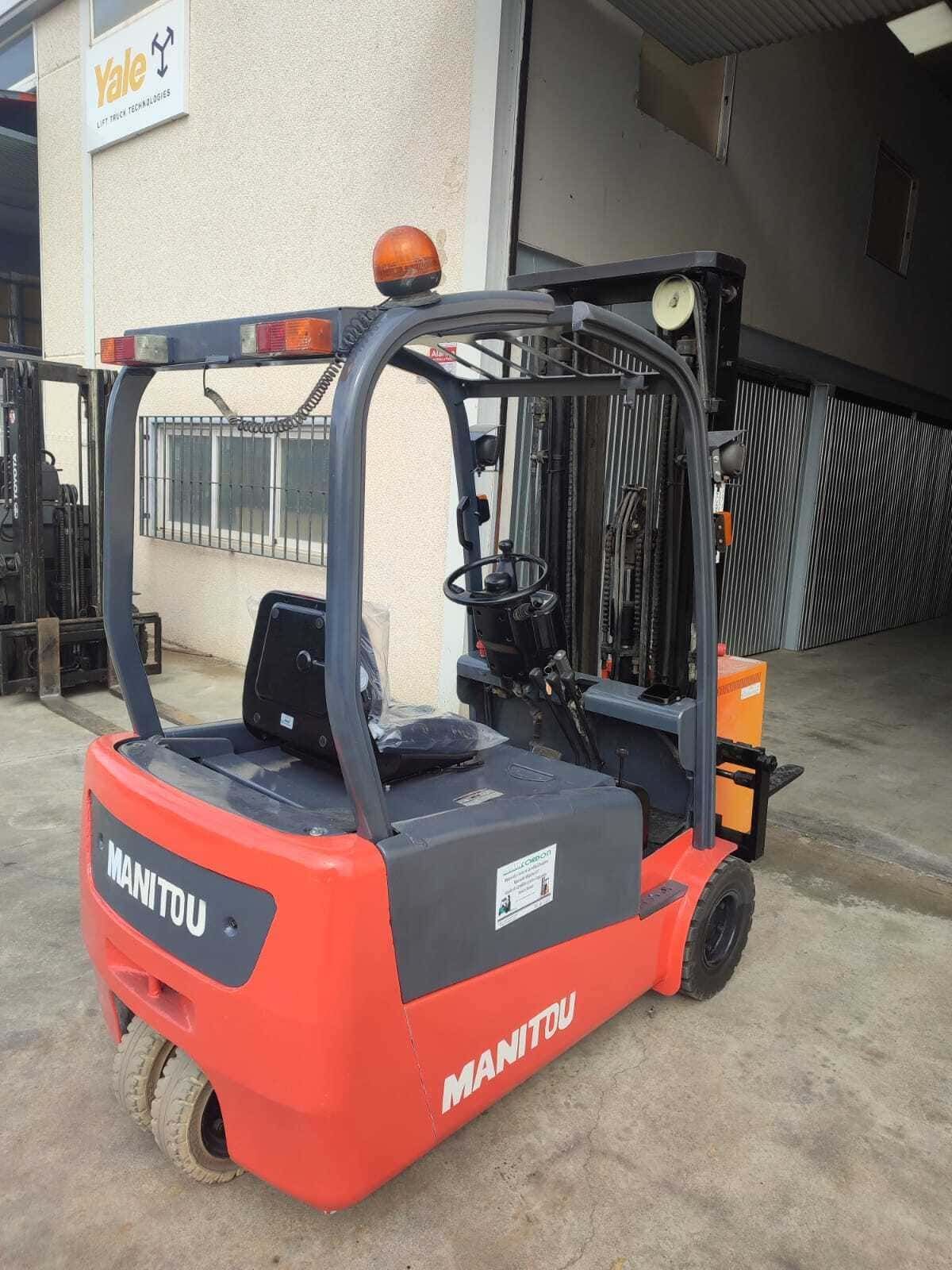 Una carretilla elevadora eléctrica Manitou de tres ruedas, de color naranja brillante, estaba estacionada frente a un edificio con una gran puerta de acceso abierta.