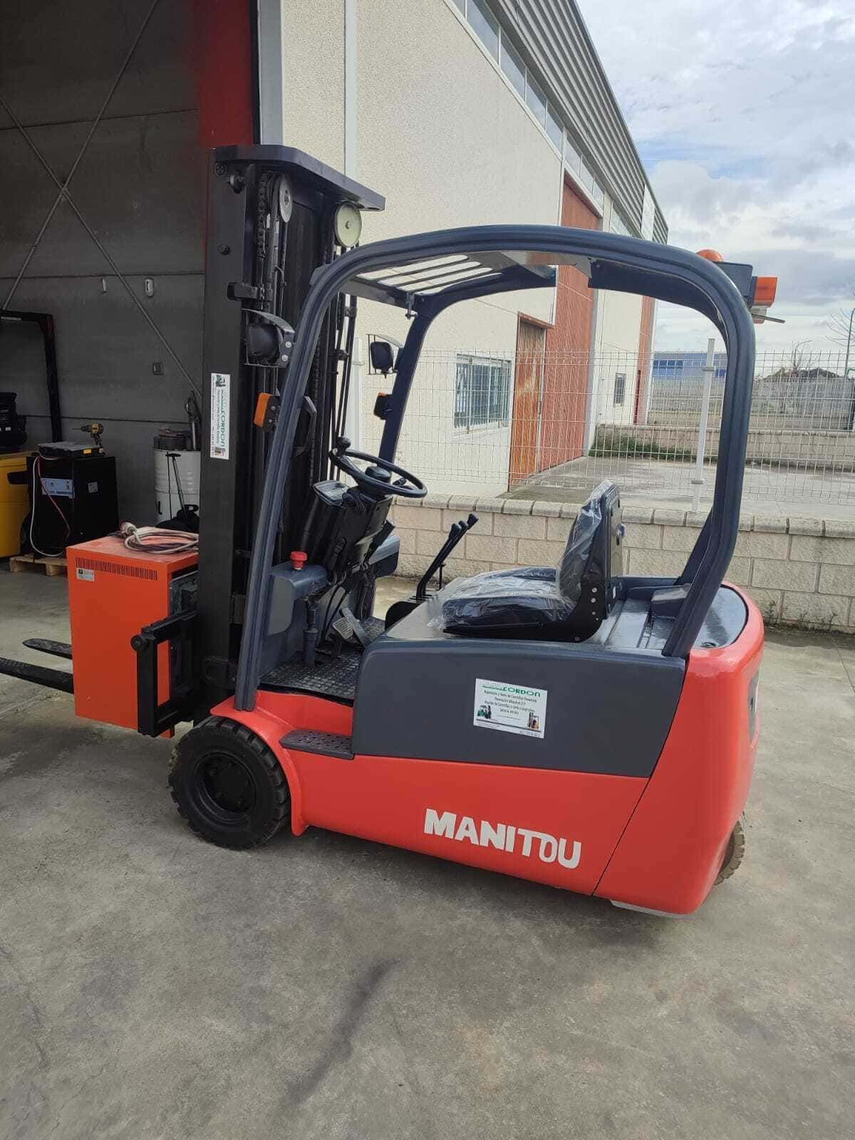 Una carretilla elevadora eléctrica Manitou de color rojo y negro estacionada sobre hormigón frente a un edificio.