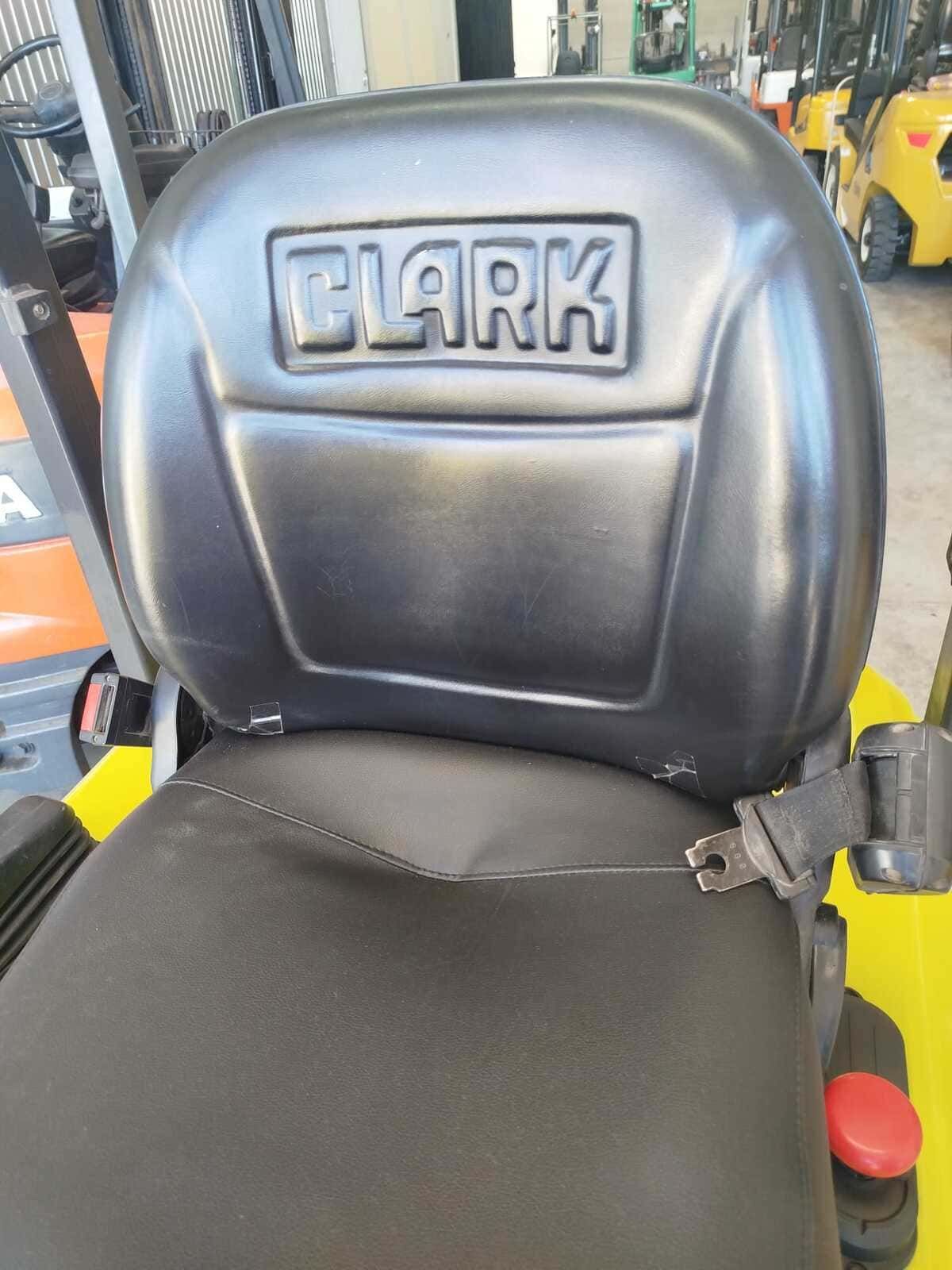 Un asiento de carretilla elevadora negro con la palabra "CLARK" grabada en el respaldo, que cuenta con un cinturón de seguridad incorporado, en un entorno de almacén.